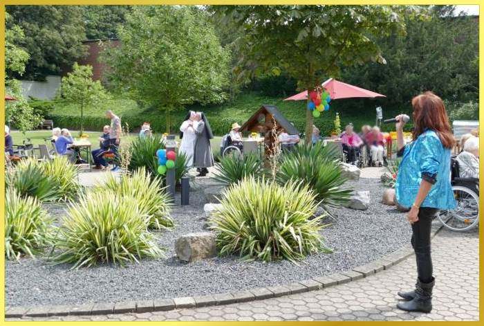 2 Nonnen tanzen im Garten. Schlagerpiratin steht ruhig am Rand der bepflanzten Mittelinsel und singt.
