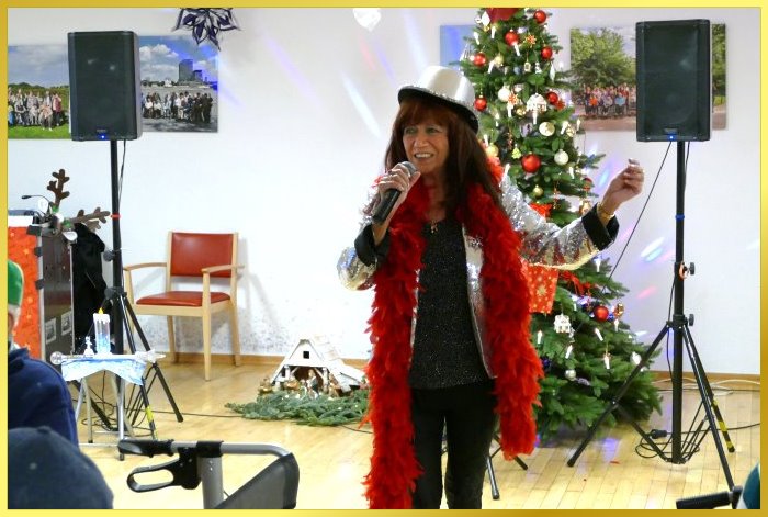 Schlagerpiratin singt Weihnachtslieder mit Boa und Hut vor dem Weihnachtsbaum