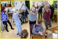 Senioren tanzen Ringelrein mit Armen nach oben.