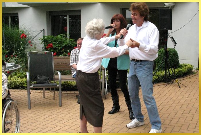 Ian und Marina singen gemeinsam und eine Seniorin tanzt mit Ian dazu. 